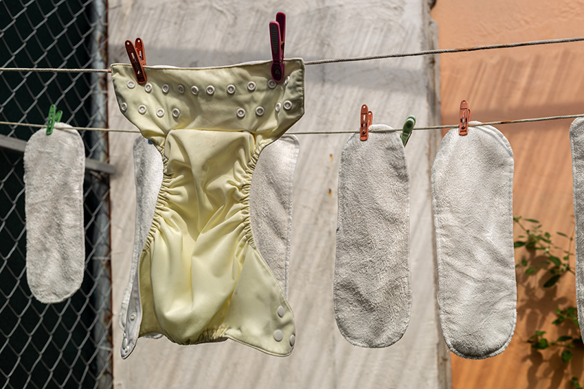 Eine gelbe Stoffwindel und Windeleinlagen hängen zum Trocknen an einer Wäscheleine.