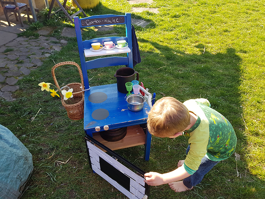 Der kleine Junge öffnet den "Backofen" der Outdoor-Spielküche.