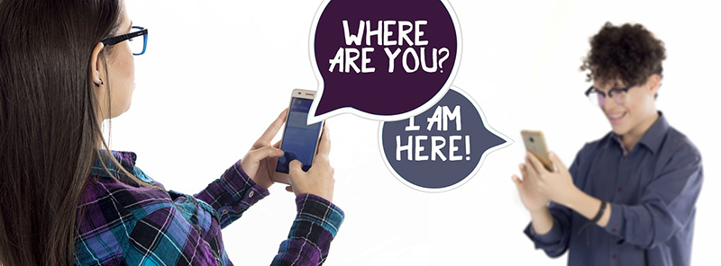 Ein Mädchen und ein Junge schreiben sich per Smartphone: Wo bist du - Ich bin hier - obwohl sie sich gegenüberstehen.