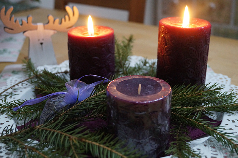 Ein Tannenzweig wird von Kerzen als Tisch-Deko begleitet