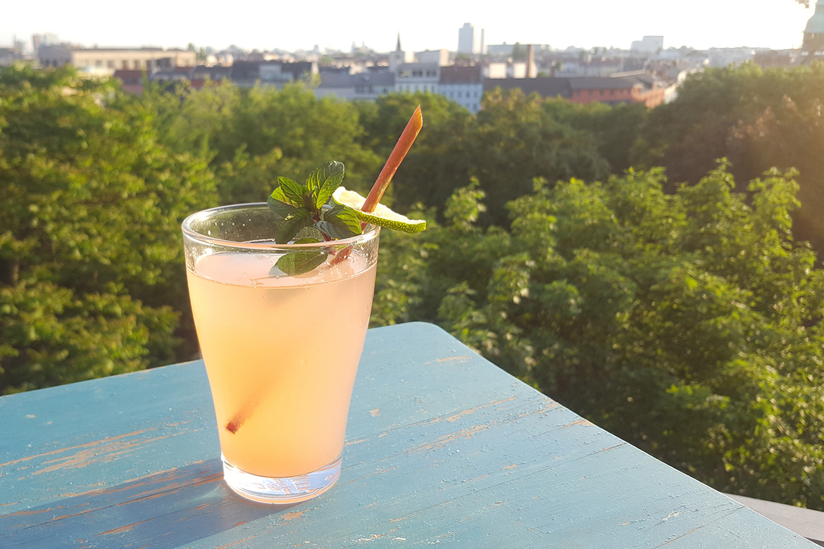 Die Rhabarber-Limo leuchtet in der Sonne, im Hintergrund öffnet sich der Ausblick vom Balkon.