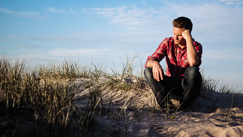 Ein Mann sitzt auf einer Sanddüne und stützt den Kopf in die Hand.