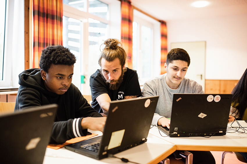 Ein MUTivator hilft zwei jungen Schülern beim Lernen am Laptop.