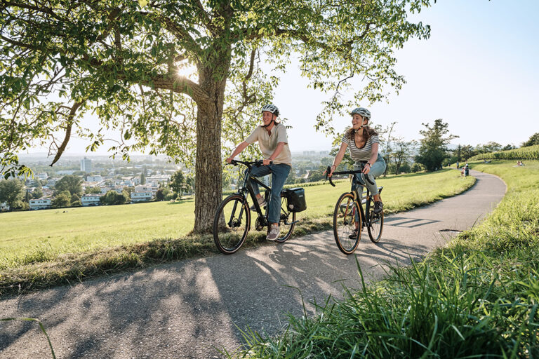Zwei Menschen fahren mit Fahrrädern und tragen beide einen Helm.
