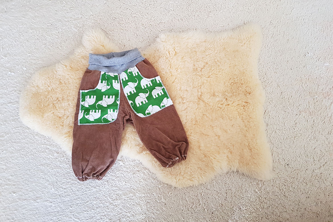 Die Upcycling-Kinderhose aus braunem Cordstoff mit Taschen aus Elefantenstoff liegt auf einem Lammfell.