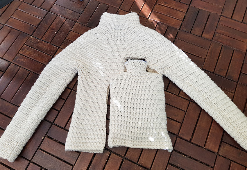 Der weiße Strickpullover liegt ausgebreitet da, die bezogene Wärmflasche liegt in der Aussparung.