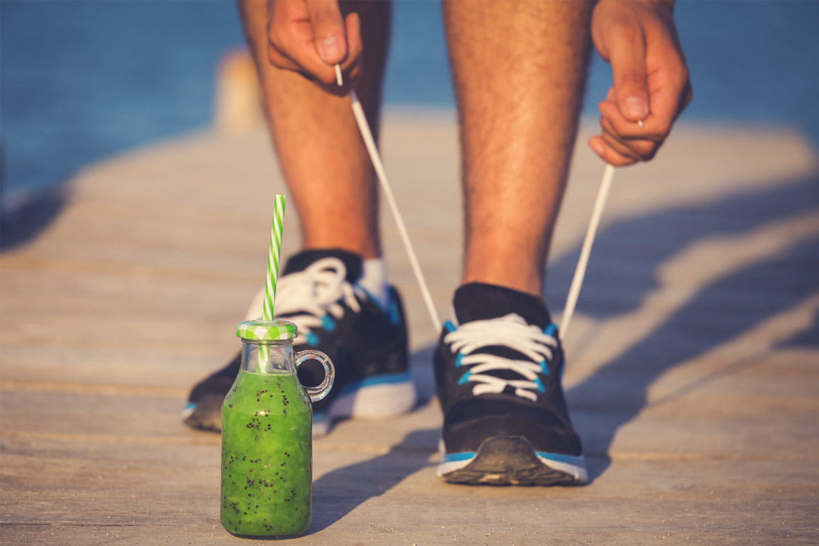 Sportler bindet sich die Schuhe, im Vordergrund ein grüner Smoothie