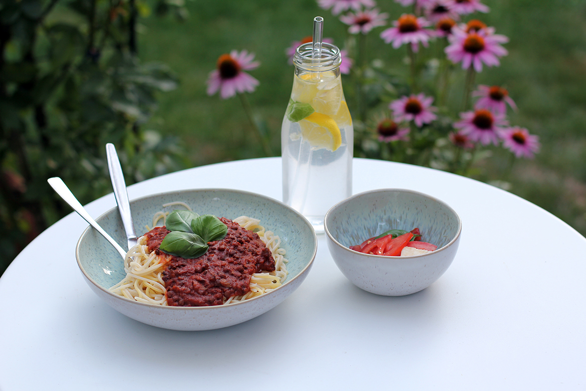 Ein Teller mit Spaghetti und der veganen Linsenbolognese, dazu ein erfrischendes Getränk und Salat.