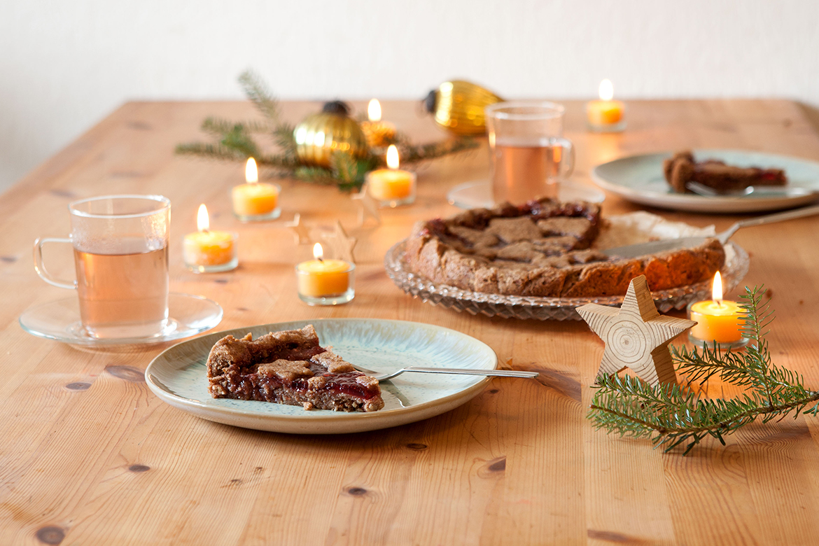 Die vegane Linzer Torte steht angeschnitten auf einem weihnachtlich gedeckten Tisch.