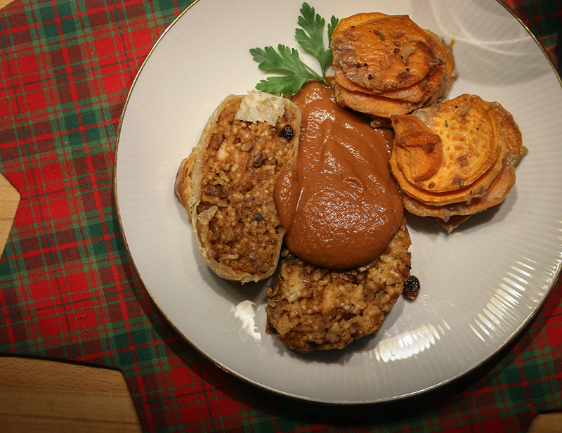 Twee plakken veganistische rollade worden geserveerd met saus en gegratineerde zoete aardappeltorentjes op een bord.