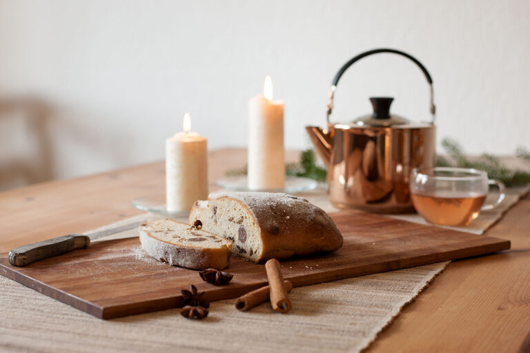 Ein veganer Quarkstollen liegt angeschnitten auf einem Holzbrett auf dem Tisch.