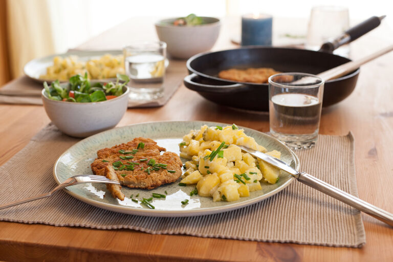 Das vegane Schnitzel aus Seitan liegt mit einer Portion Kartoffelsalat auf einem Teller.