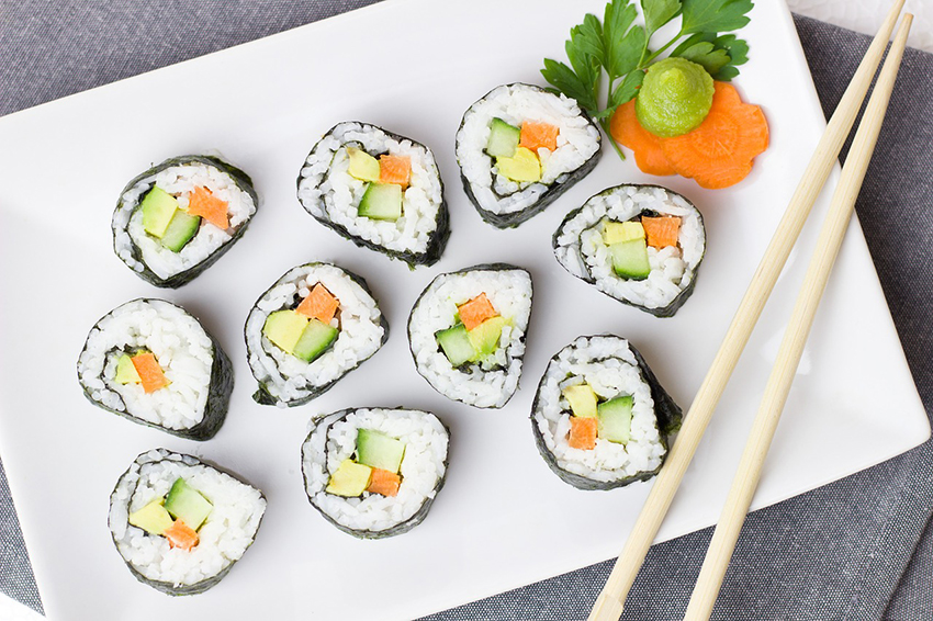 Mit Gemüse gefüllte Sushi-Röllchen lieben auf einem Teller, zwei Essstäbchen sind auch parat.