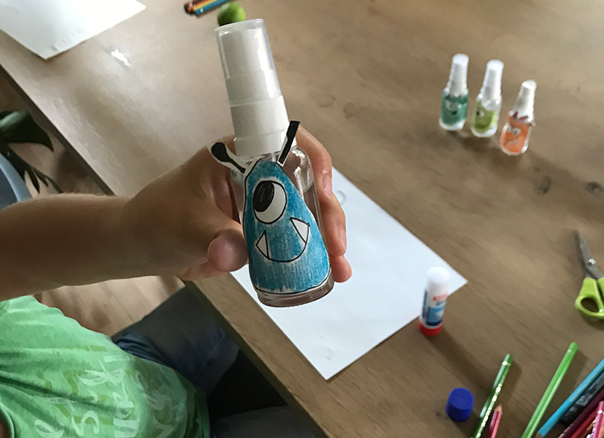 Die Kinderhand hält die Sprühflasche mit aufgeklebtem blauen Monster in die Kamera.