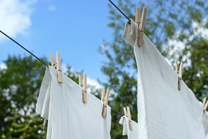 Eine Wäscheleine im Garten mit aufgehängten weißen Textilien.