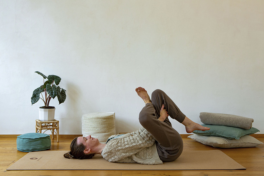 Die Yogalehrerin Lea liegt mit dem Rücken auf einer Korkmatte und macht Yoga im Homeoffice.