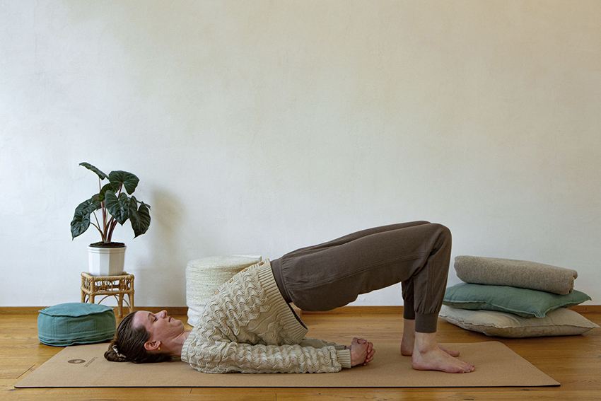 Yogalehrerin Lea in der Schulterbrücke, die Übung führt sie auf einer Yogamatte aus Kork durch.