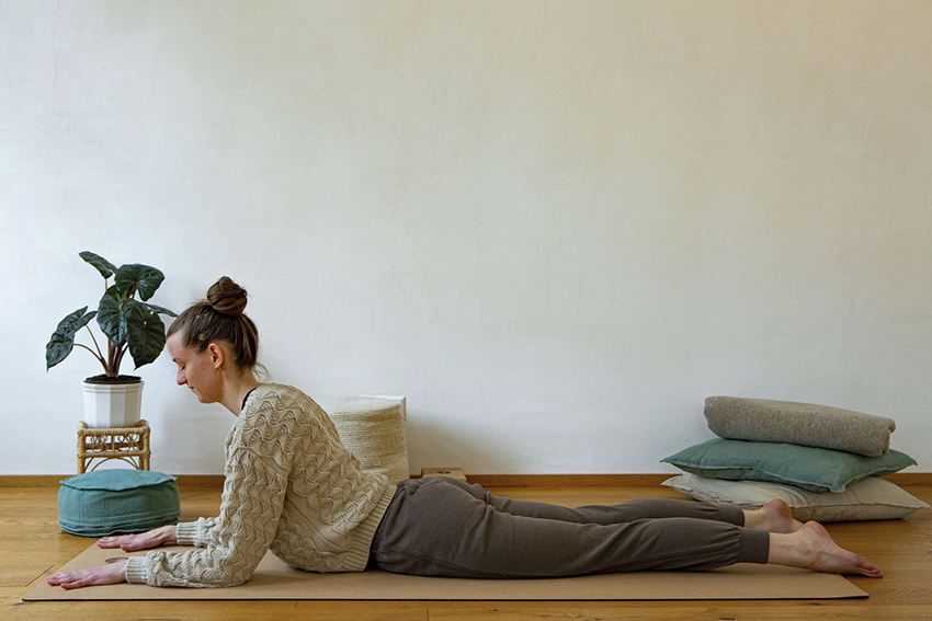 Yogalehrerin Lea liegt mit dem Bauch auf einer Yogamatte und stützt sich auf ihren Unterarmen ab.