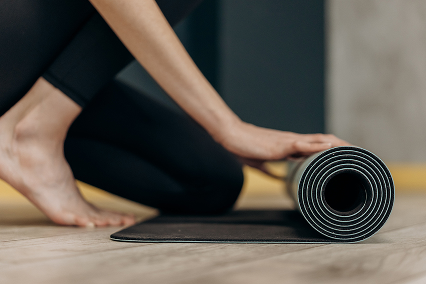 Yogamatte wird kniend auf dem Boden ausgerollt.