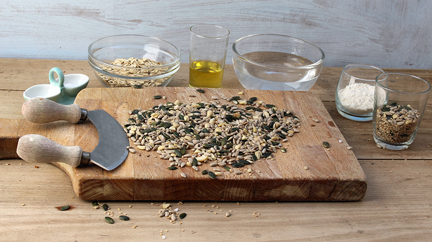 De ingrediënten voor het zelfgemaakte knäckebröd staan in schaaltjes rond een houten plank. 