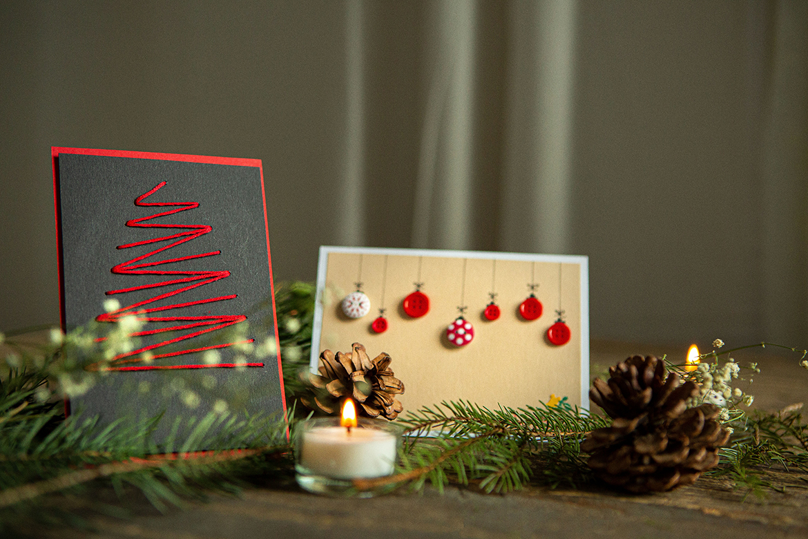 Zwei selbst gebastelte Weihnachtskarten sind auf einem weihnachtlich geschmücktem Tisch aufgestellt.