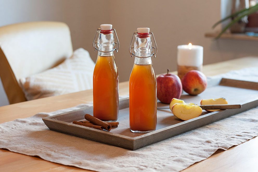Selbst gemachter Apfel-Zimt-Likör steht in zwei Flaschen abgefüllt auf einem Holzbrett auf dem dekorierten Tisch.