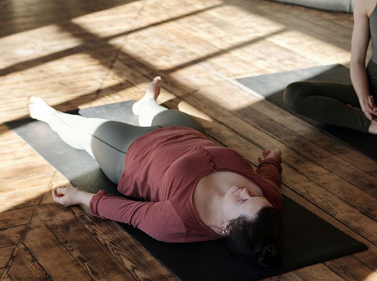 Zwei Frauen führen in einem Yogastudio eine Body-Scan-Meditation durch.