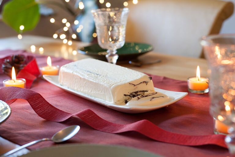 Das Parfait steht bereits angeschnitten auf einem weihnachtlich gedeckten Tisch.