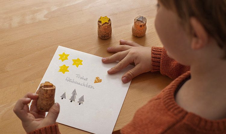 Die Stempel aus Korken werden von einem kleinen Jungen benutzt, der damit eine Weihnachtskarte verziert.