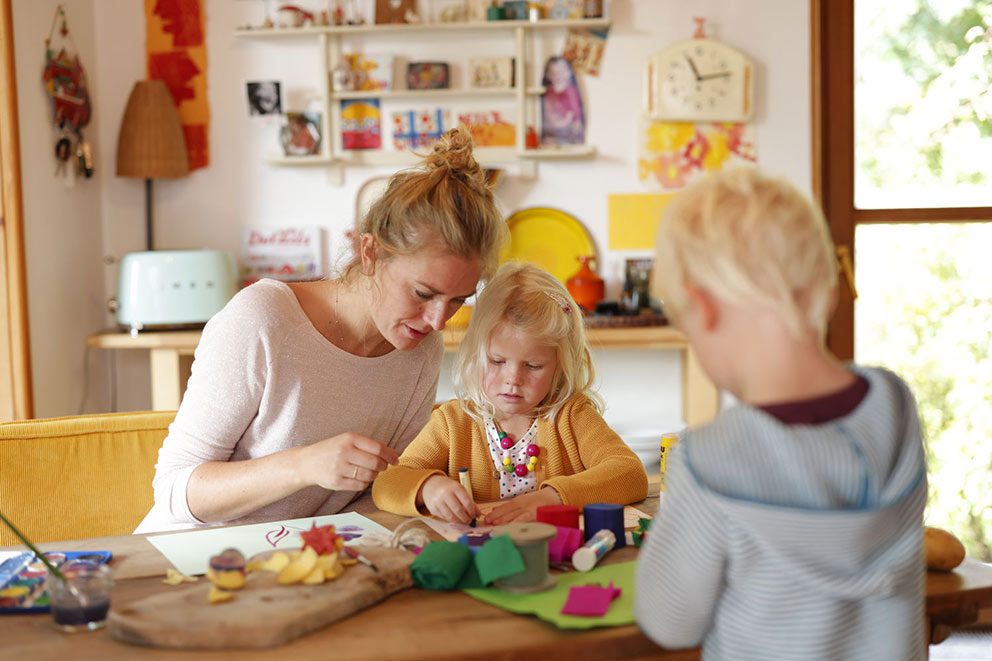 Eine Mutter sitzt mit ihren zwei Kindern an einem Tisch und bastelt.