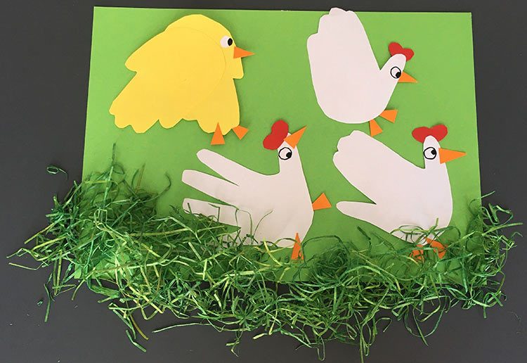 Beim Basteln mit Kleinkindern sind niedliche Hühner aus ausgeschnittenen Händen entstanden, die auf eine grüne Pappe geklebt wurden.