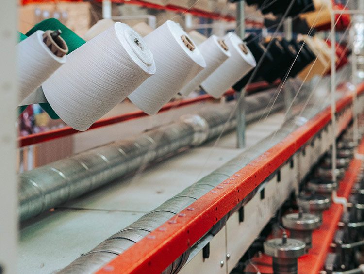 Ein Kunstfasergarn wird in einer Kleidungsfabrik verarbeitet, um mit Mikroplastik in Kleidung die Klamotten bequemer zu machen.