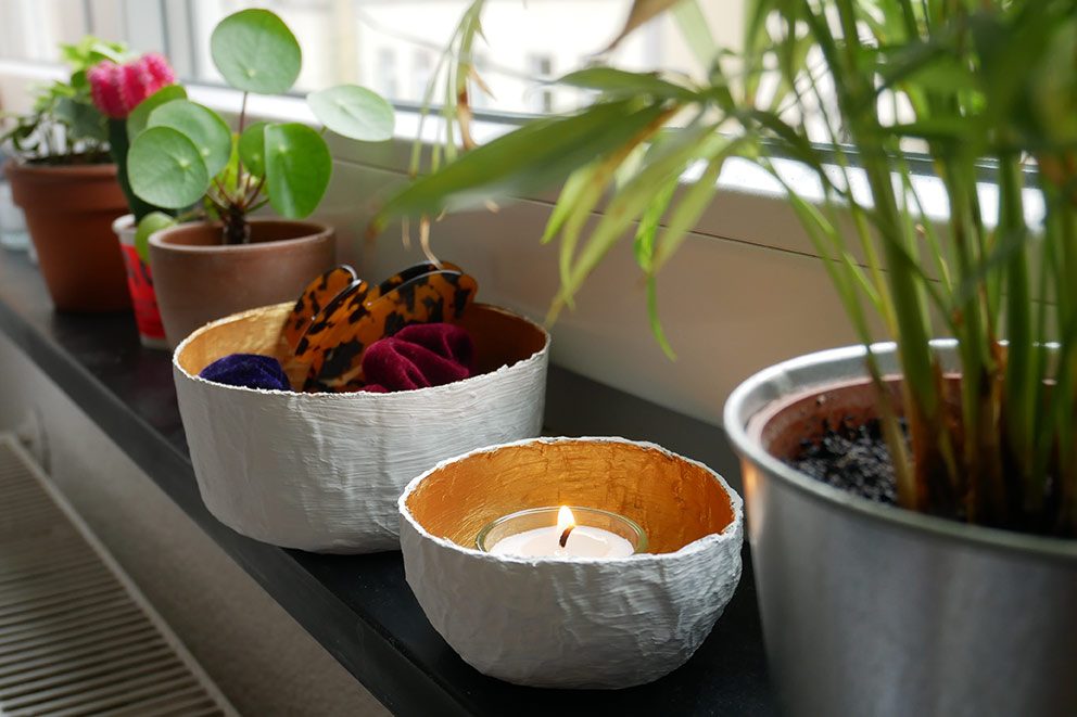 Selbst gebastelte Schalen aus Pappmaché stehen mit einigen Pflanzen auf einer Fensterbank.