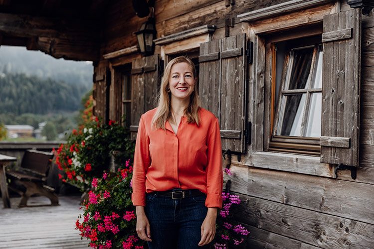 Katharina Afflerbach vor einer hübschen Berghütte im Porträt.