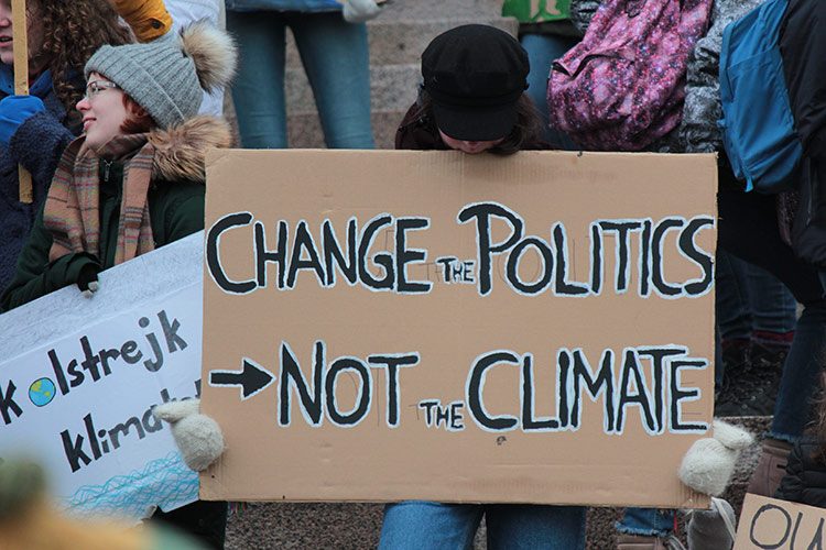 Auf einer Klimademonstration wird mit einem Schild für politische Veränderungen und Klimagerechtigkeit demonstriert.