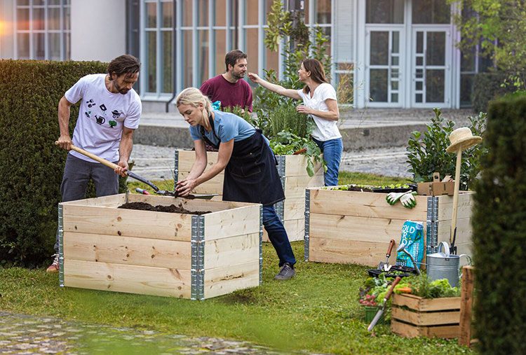 Eine Gruppe befüllt Hochbeete mit Gartenerde.