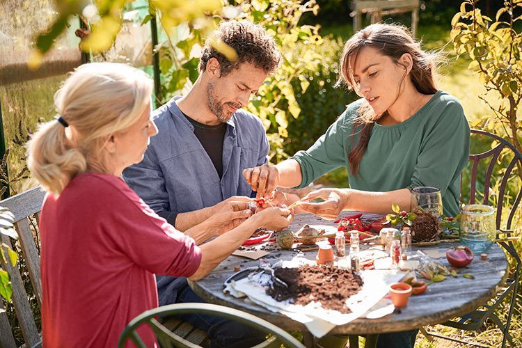 Drie mensen zitten aan een tuintafel en ruilen zaad dat ze zelf hebben geoogst.