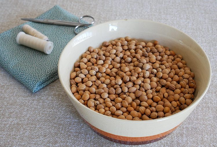 Eine Schale mit gesammelten Kirschkernen steht neben dem Stoff für das Kirschkernkissen.