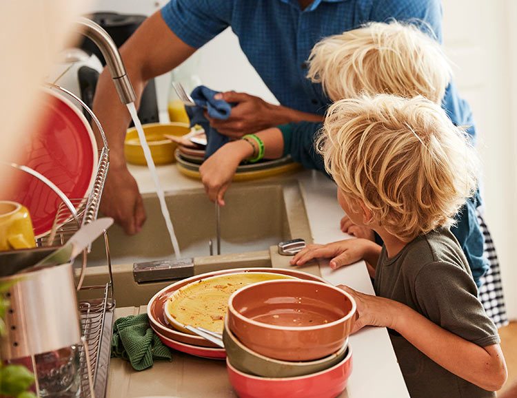 Zwei kleine Kinder helfen beim Geschirrspülen.