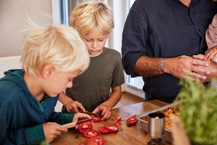 Zwei Jungen schneiden mit Allzweckmessern Tomaten für einen Salat.