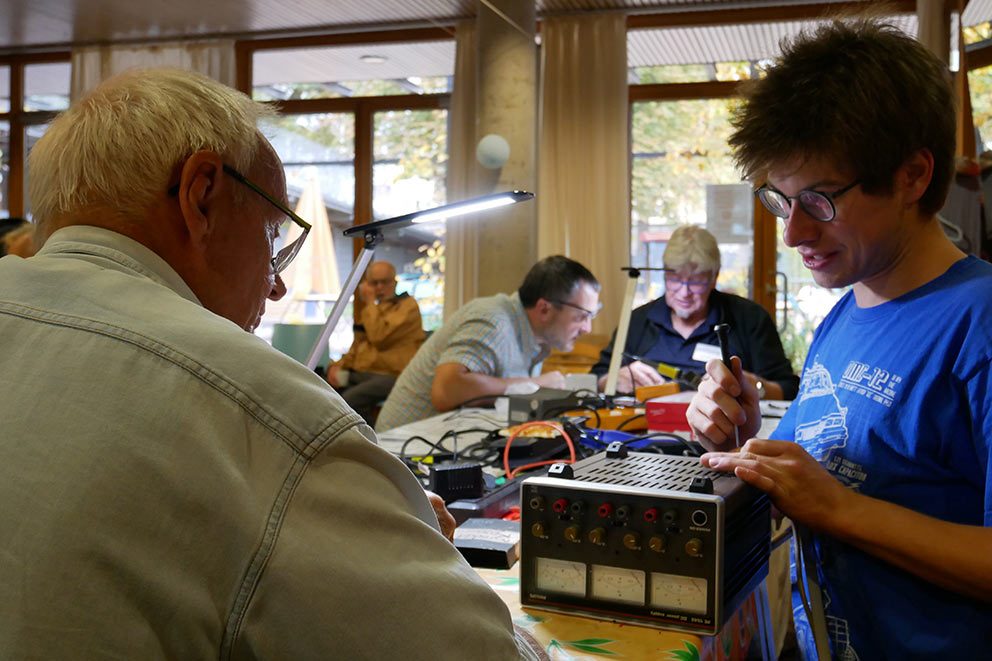 Zwei Männer reparieren gemeinsam im Repair Café ein altes Elektrogerät.