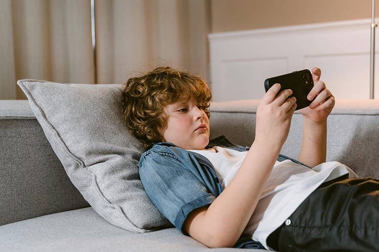 Ein Junge liegt auf seinem Bett und benutzt sein Handy.