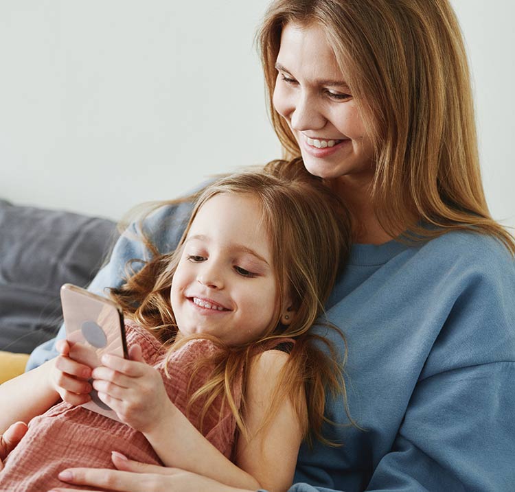 Eine Mutter zeigt ihrer Tochter beim ersten Handy für Kinder, wie es zu bedienen ist.