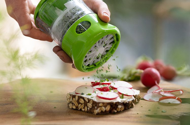 In Scheiben geschnittene Radieschen liegen auf einer Scheibe Brot, auf die frische Kräuter gegeben werden.