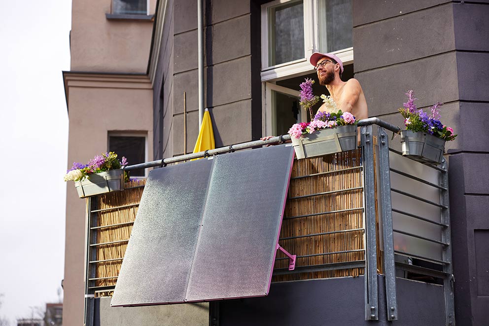 Ein Mann steht auf seinem Balkon, an dem ein Balkonkraftwerk angebracht ist.