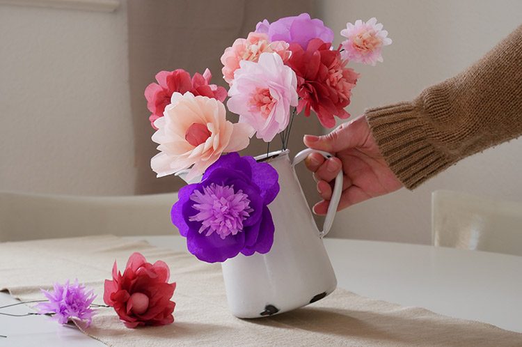 Eine Kanne mit verschiedenen Papierblumen wird auf den Esstisch gestellt.