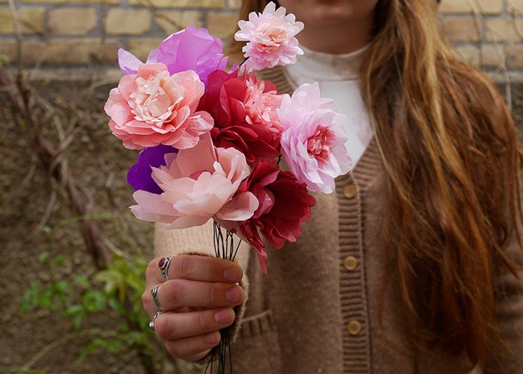 Een vrouw houdt voor zich een boeket zelfgemaakte papieren bloemen vast.