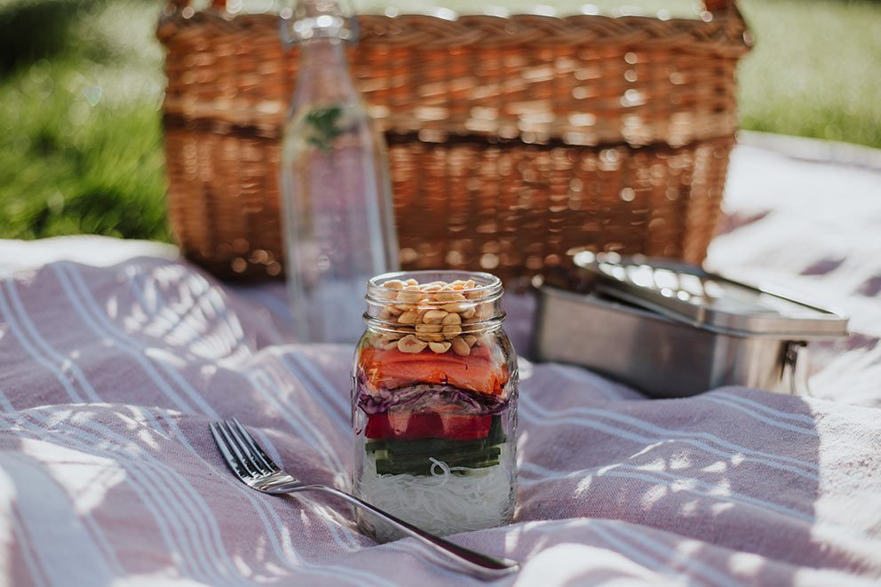 Ein vorgerichteter Salat im Glas steht auf einer Picknickdecke.