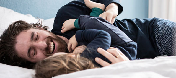 Vater und Kind toben in Pyjamas auf dem Bett