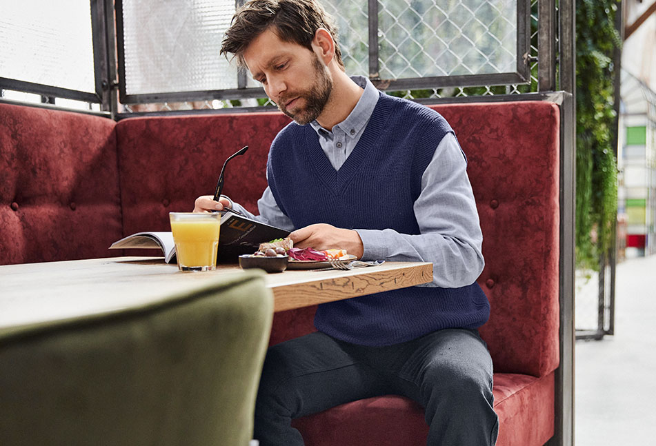Mann in Hanf-Kleidung sitzt in einem Bistro und liest eine Zeitschrift.